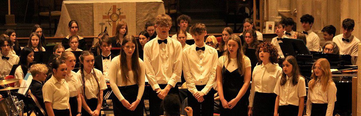 Group of children standing singing with young musicians playing behind them