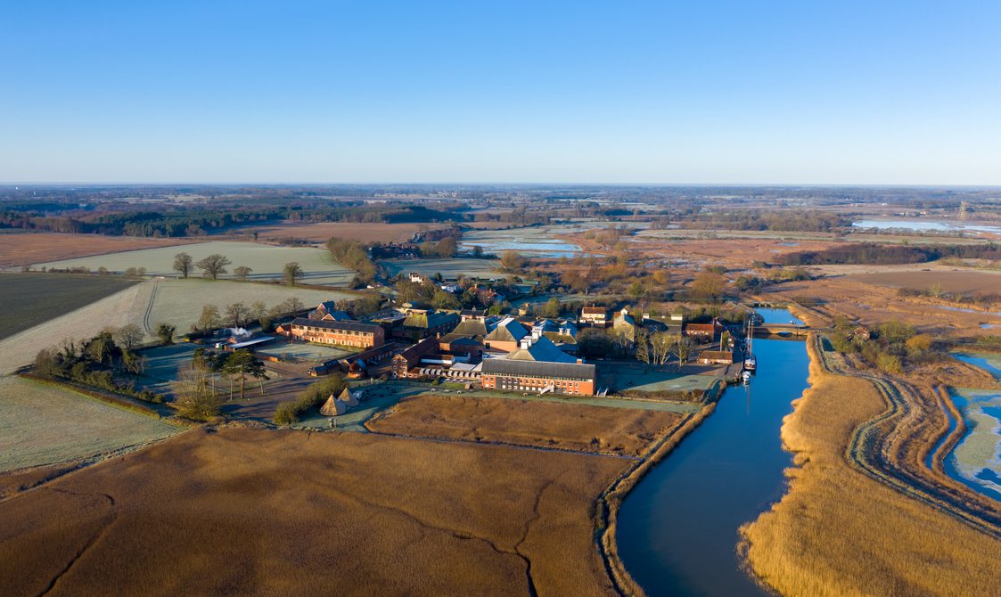 Aerial view of Snape Maltings buildings, surrounded by fields and the winding River Alde.